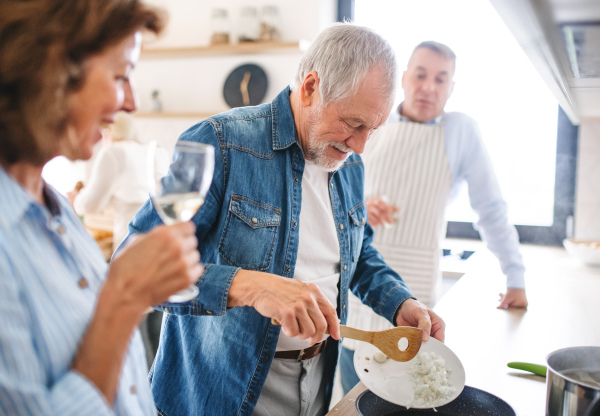 Front view of group of cheerful senior friends at dinner party at home, cooking.