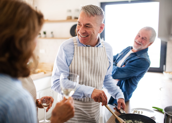 Front view of group of cheerful senior friends at dinner party at home, cooking.