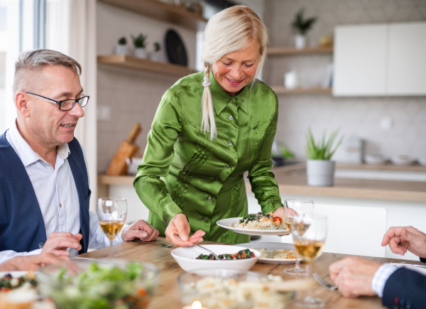 Group of senior friends enjoying dinner party at home, eating.