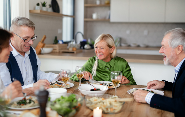 Group of senior friends enjoying dinner party at home, eating.