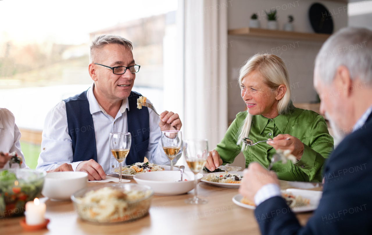 Group of senior friends enjoying dinner party at home, eating.