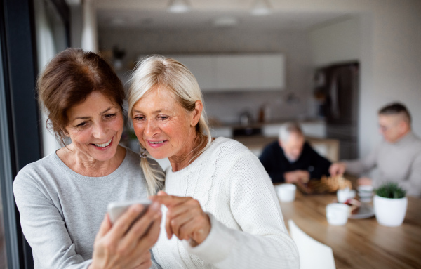 A group of senior friends at home, using smartphones.