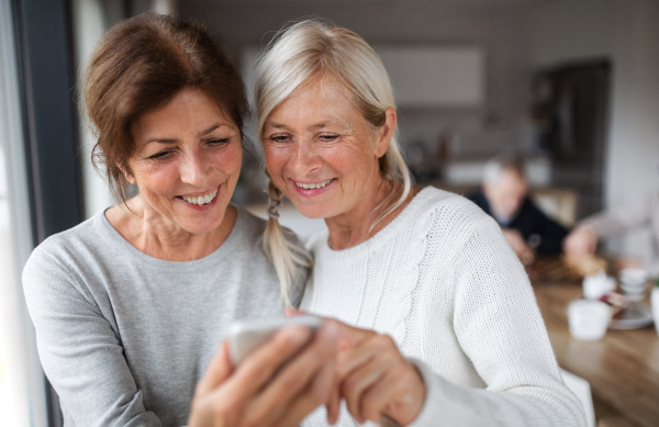 A group of senior friends at home, using smartphone.