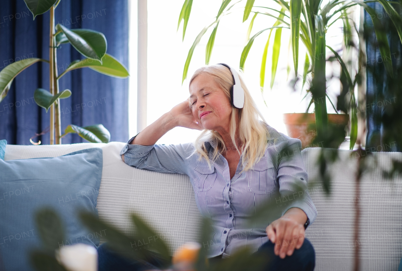 Happy attractive senior woman with headphones sitting indoors on sofa, relaxing.