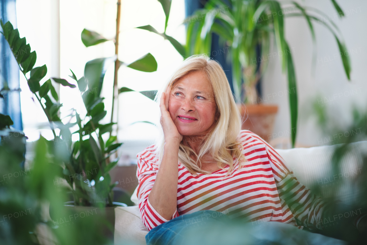 Front view of attractive senior woman sitting indoors on sofa, resting.