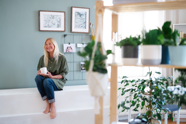 Attractive senior woman with coffee sitting indoors at home, resting. Copy space.