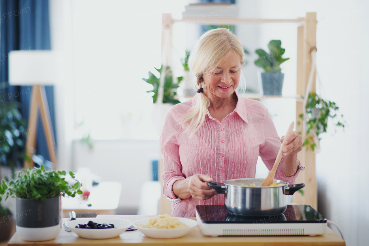 Front view of senior woman cooking in kitchen indoors, stirring pasta in pot.