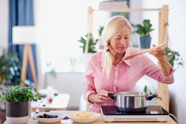 Front view of senior woman cooking in kitchen indoors, stirring pasta in pot.