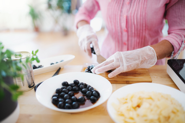 Unrecognizable woman with gloves cooking in kitchen indoors, chopping. Hygiene concept.