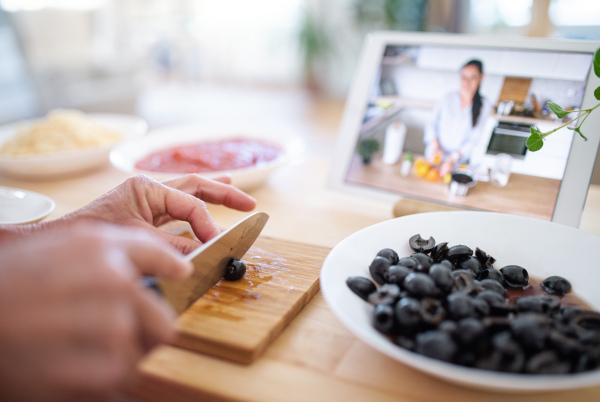 Unrecognizable senior woman preparing food in kitchen indoors, following food vlogger on tablet.