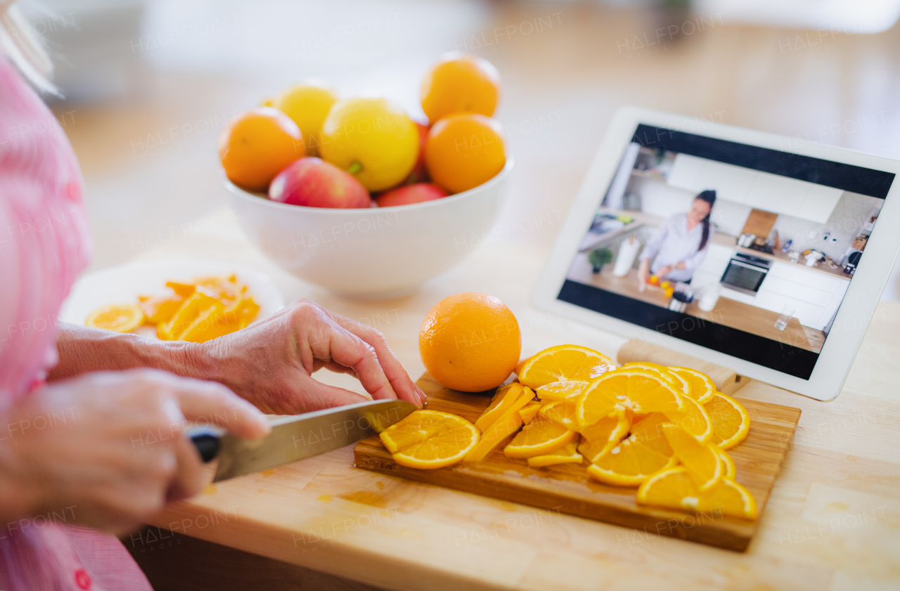 Unrecognizable senior woman preparing food in kitchen indoors, following food vlogger on tablet.