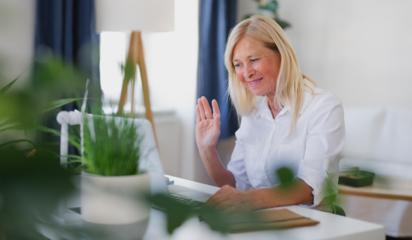 Senior businesswoman with laptop sitting indoors in home office, business call concept.