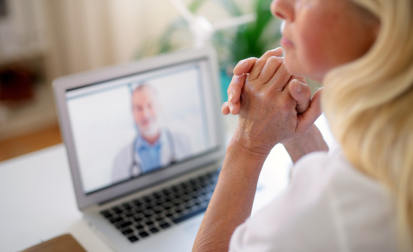 Senior woman with laptop indoors at home, consulting doctor and video call concept.