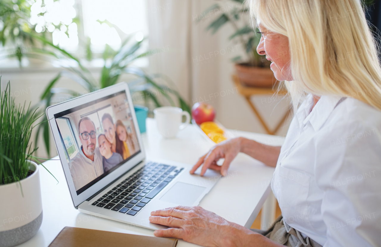 Happy senior woman with laptop indoors at home, family video call concept.