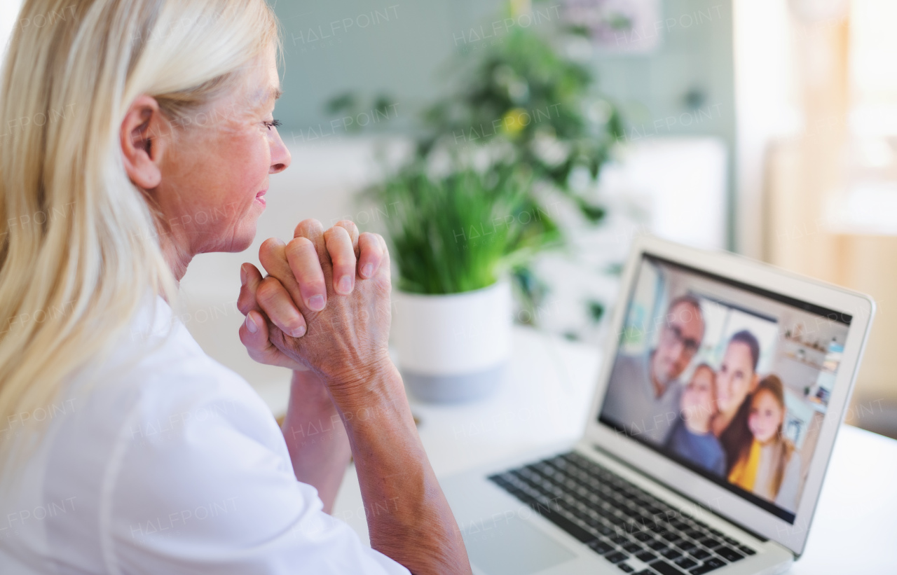 Happy senior woman with laptop indoors at home, family video call concept.