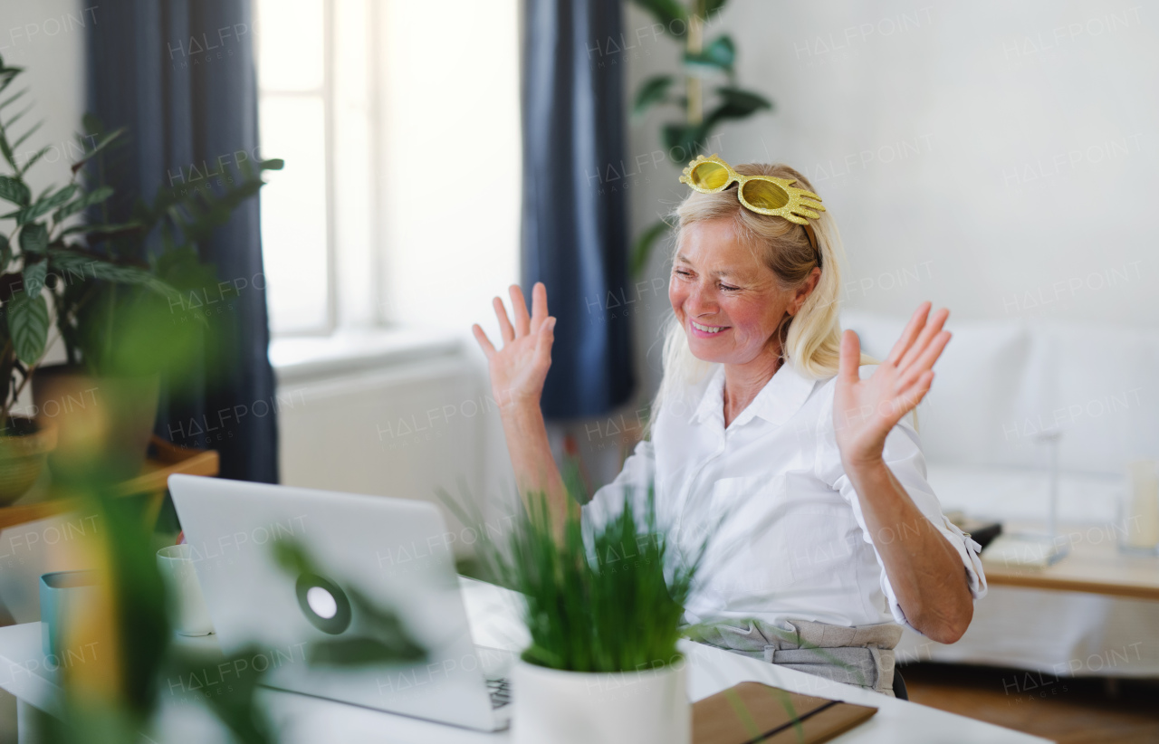 Happy senior woman with laptop indoors at home, family video call concept.