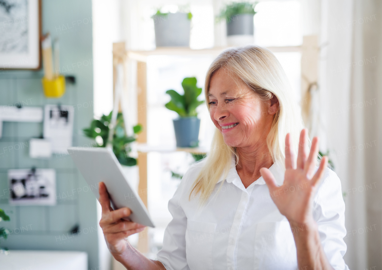 Happy senior businesswoman with tablet indoors in home office, business call concept.