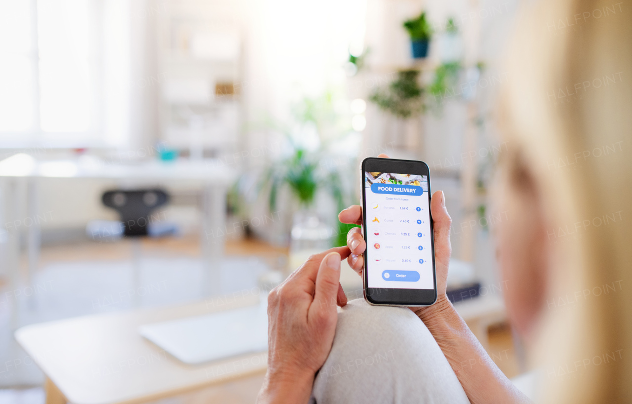 Unrecognizable woman with smartphone indoors at home, ordering food online.