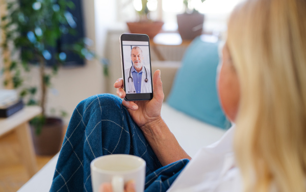 Senior woman with smartphone indoors at home, consulting doctor and video call concept.