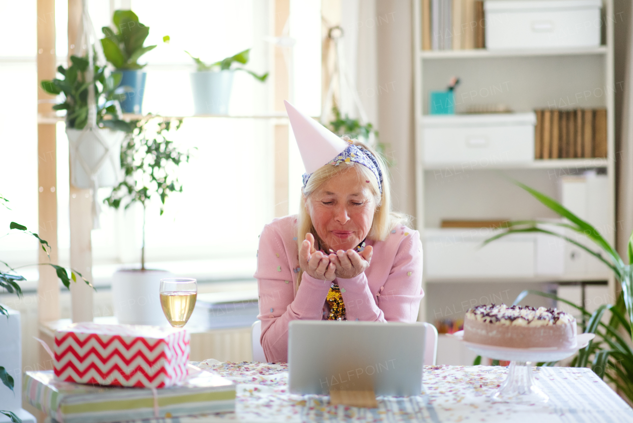 Senior woman with laptop, cake and wine indoors at home, celebrating distance birthday.