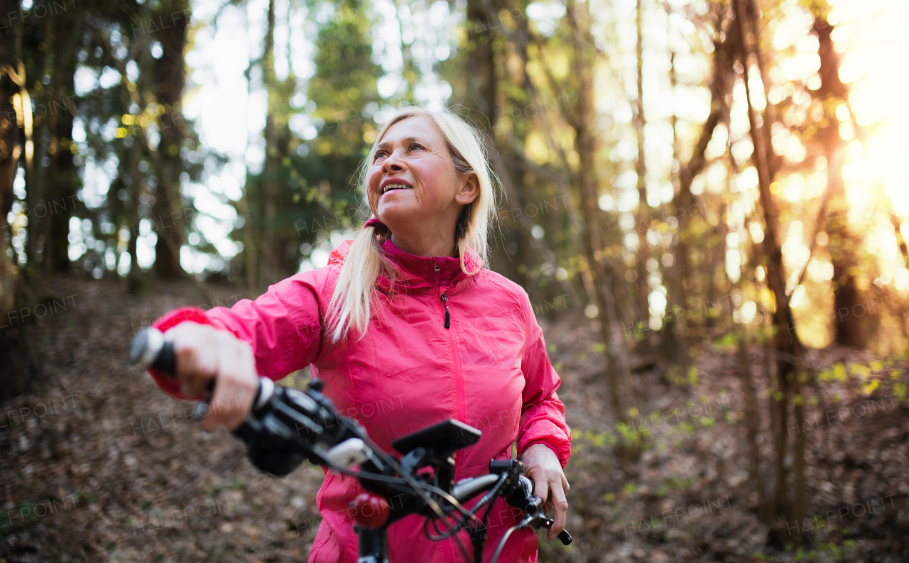 Active senior woman with e-bike cycling outdoors in forest in nature. Copy space.