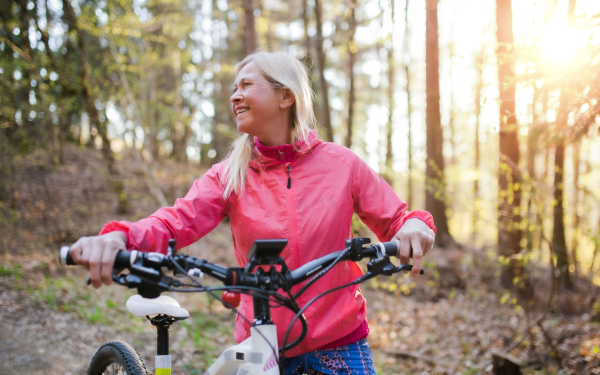 Active senior woman with e-bike cycling outdoors in nature. Copy space.