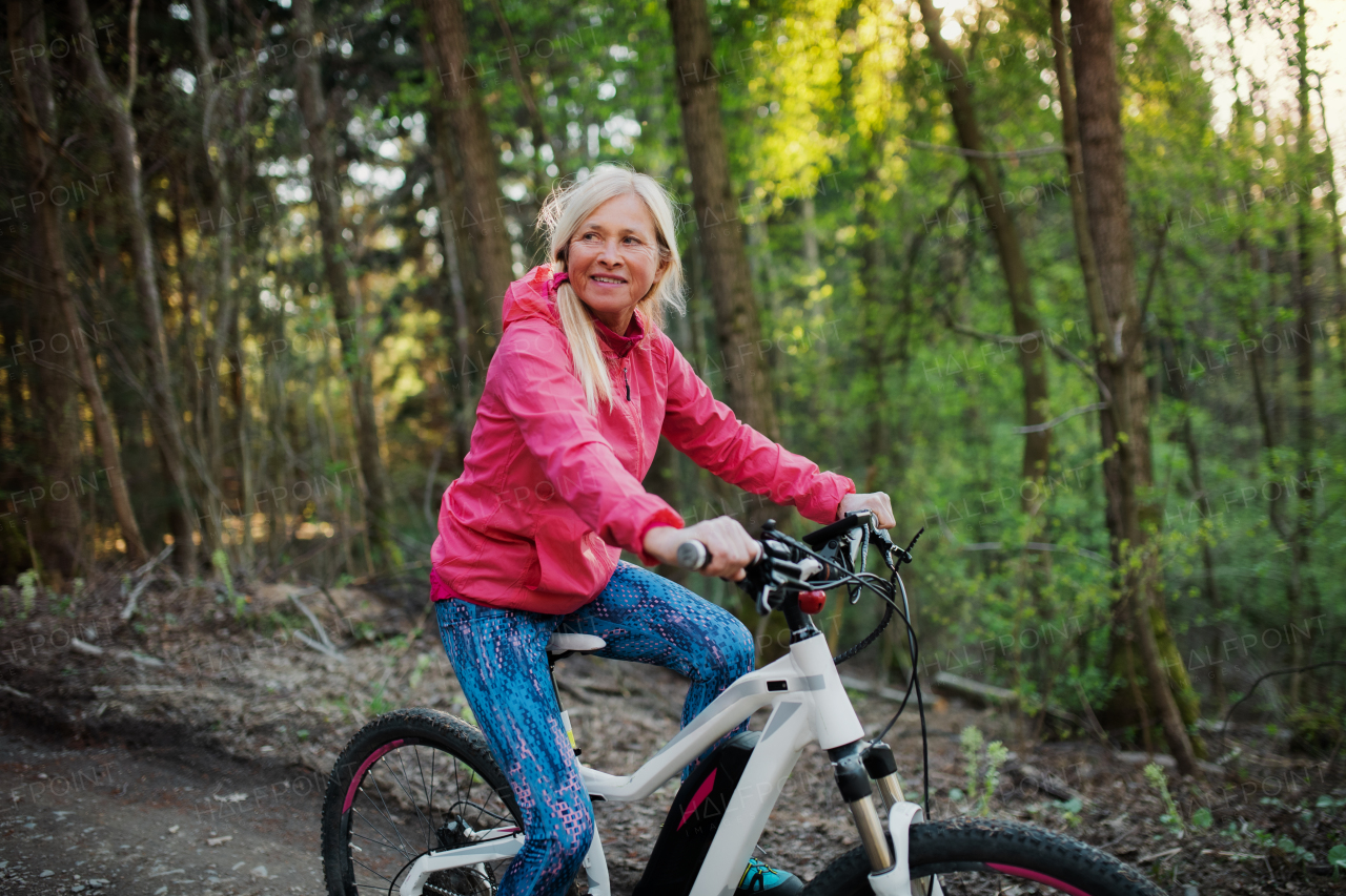 Active senior woman with e-bike cycling outdoors in nature. Copy space.