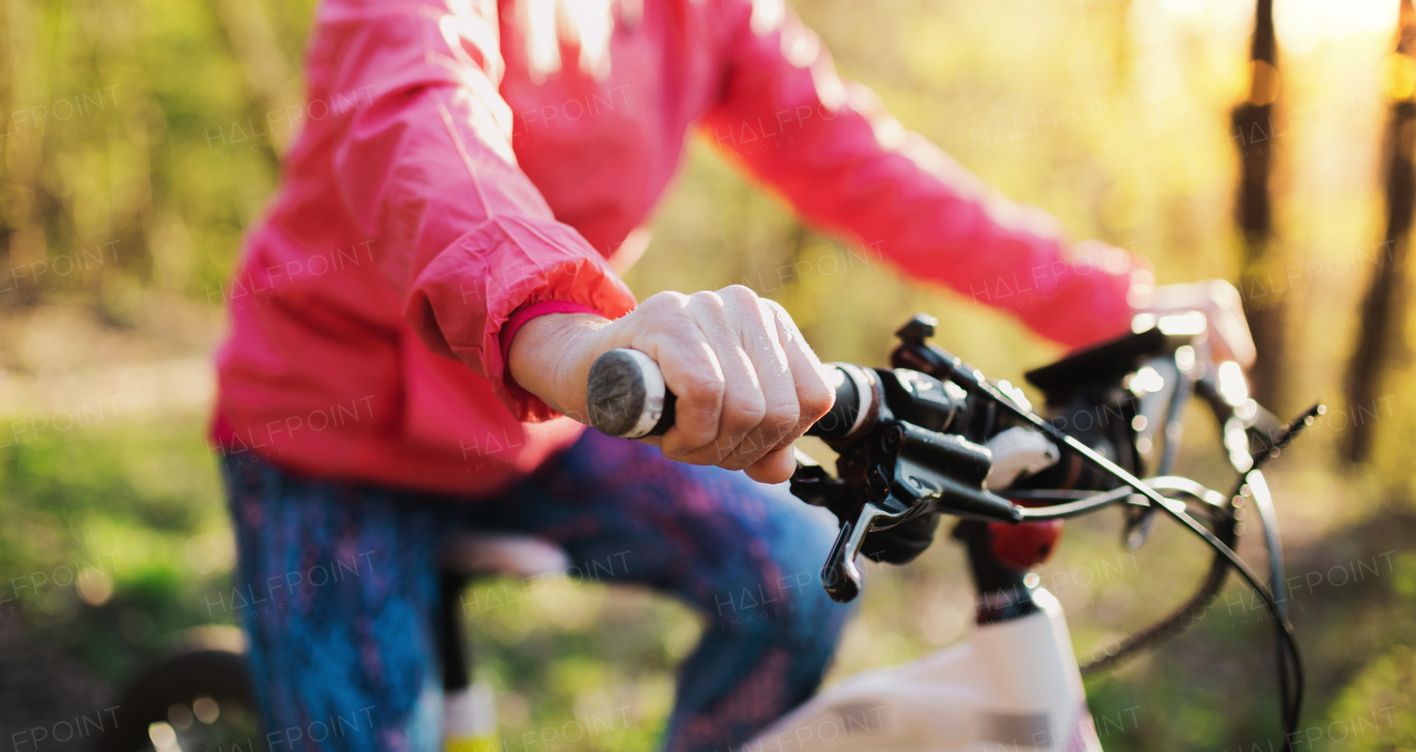 Unrecognizable active senior woman with bicycle cycling outdoors in nature.