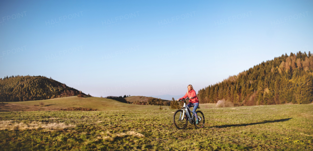 Active senior woman with e-bike cycling outdoors in nature. Copy space.