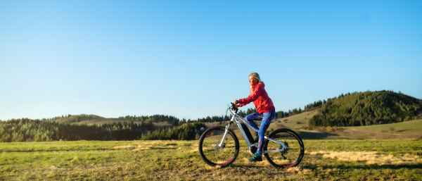 Active senior woman with e-bike cycling outdoors in nature. Copy space.