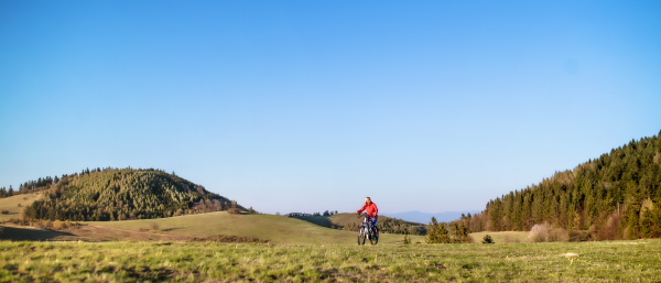 Active senior woman with e-bike cycling outdoors in nature. Copy space.