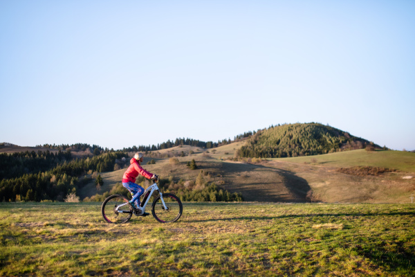 Active senior woman with e-bike cycling outdoors in nature. Copy space.