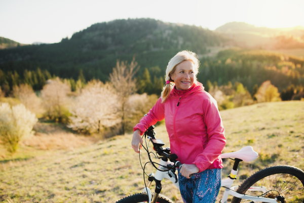 Active senior woman with bicycle outdoors in nature, resting. Copy space.