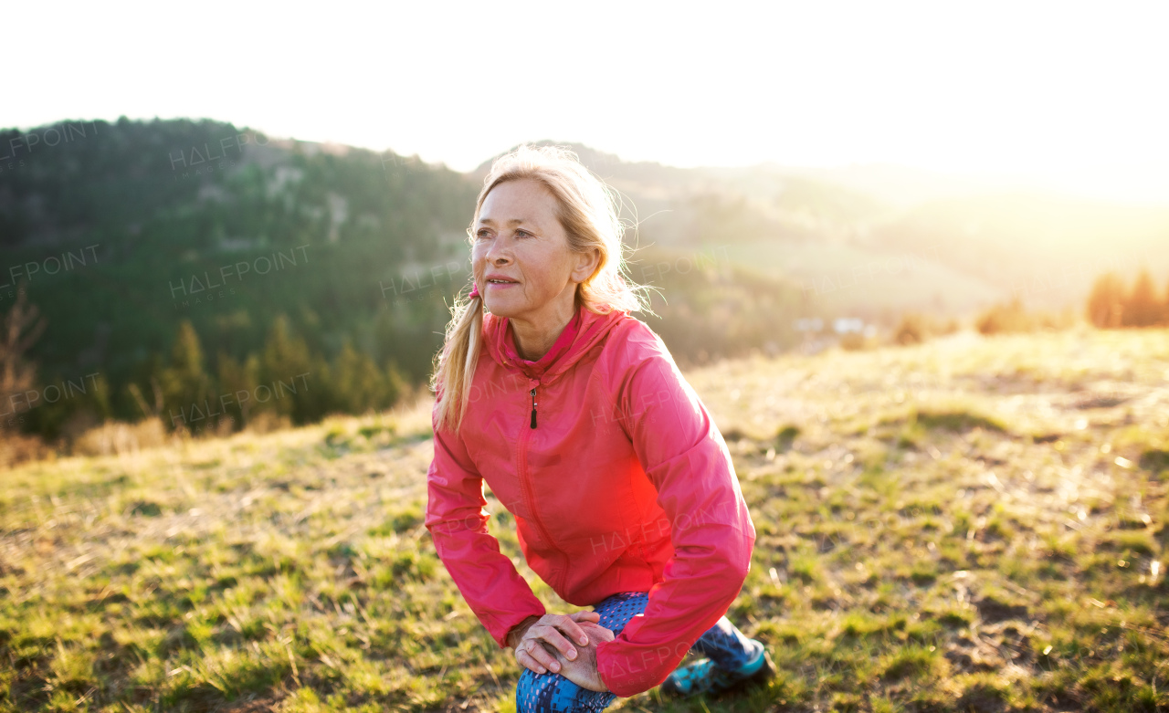 Attractive senior woman doing exercise outdoors in nature at sunset, stretching.