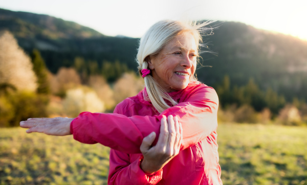 Happy attractive senior woman doing exercise outdoors in nature, stretching.