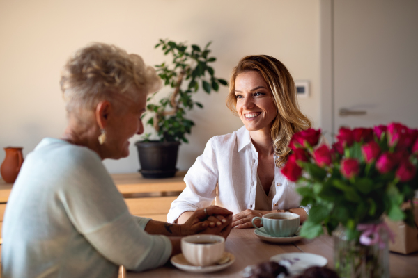 A happy senior mother having coffee with adult daughter indoors at home, sitting and talking.