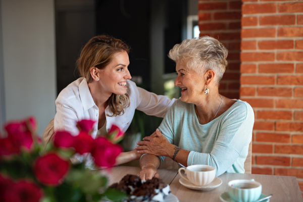 A happy senior mother having coffee with adult daughter indoors at home, sitting and talking.