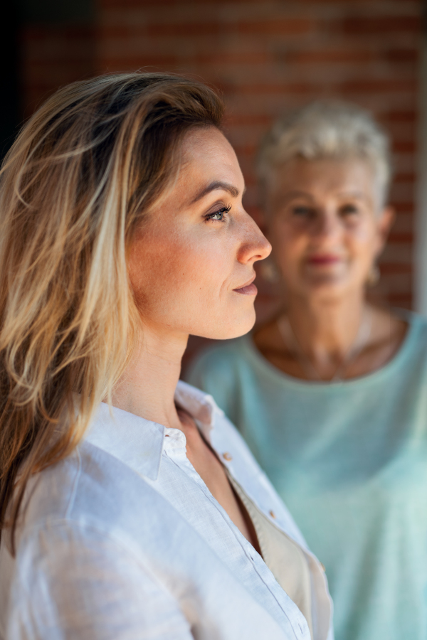 A senior mother looking at her adult daughter indoors at home. Selective focus on woman in foreground.