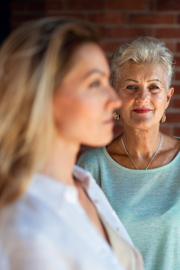 A senior mother looking at her adult daughter indoors at home. Selective focus on woman in background.