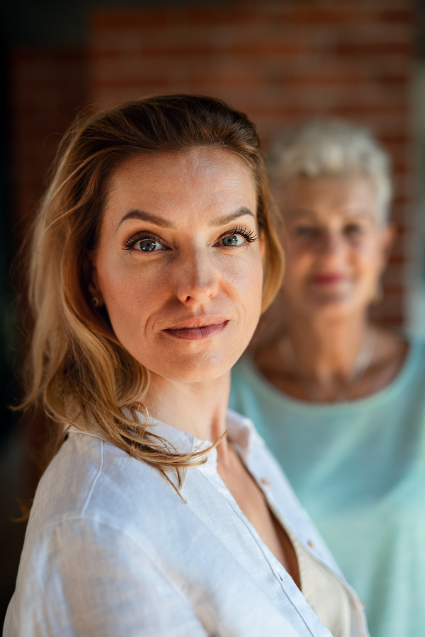 A young woman looking at camera, her mother at background looking at her .