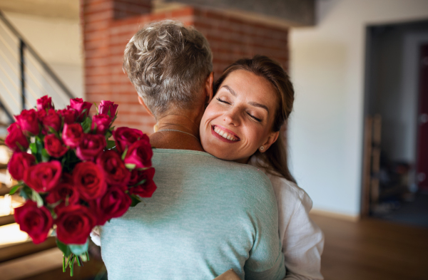 A happy senior mother hugging adult daughter indoors at home, mothers day or birthday celebration.