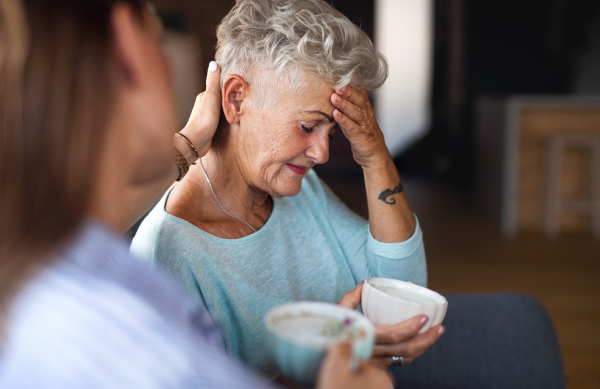 An adult daughter consoling unhappy senior mother and supporting her in struggle indoors at home.