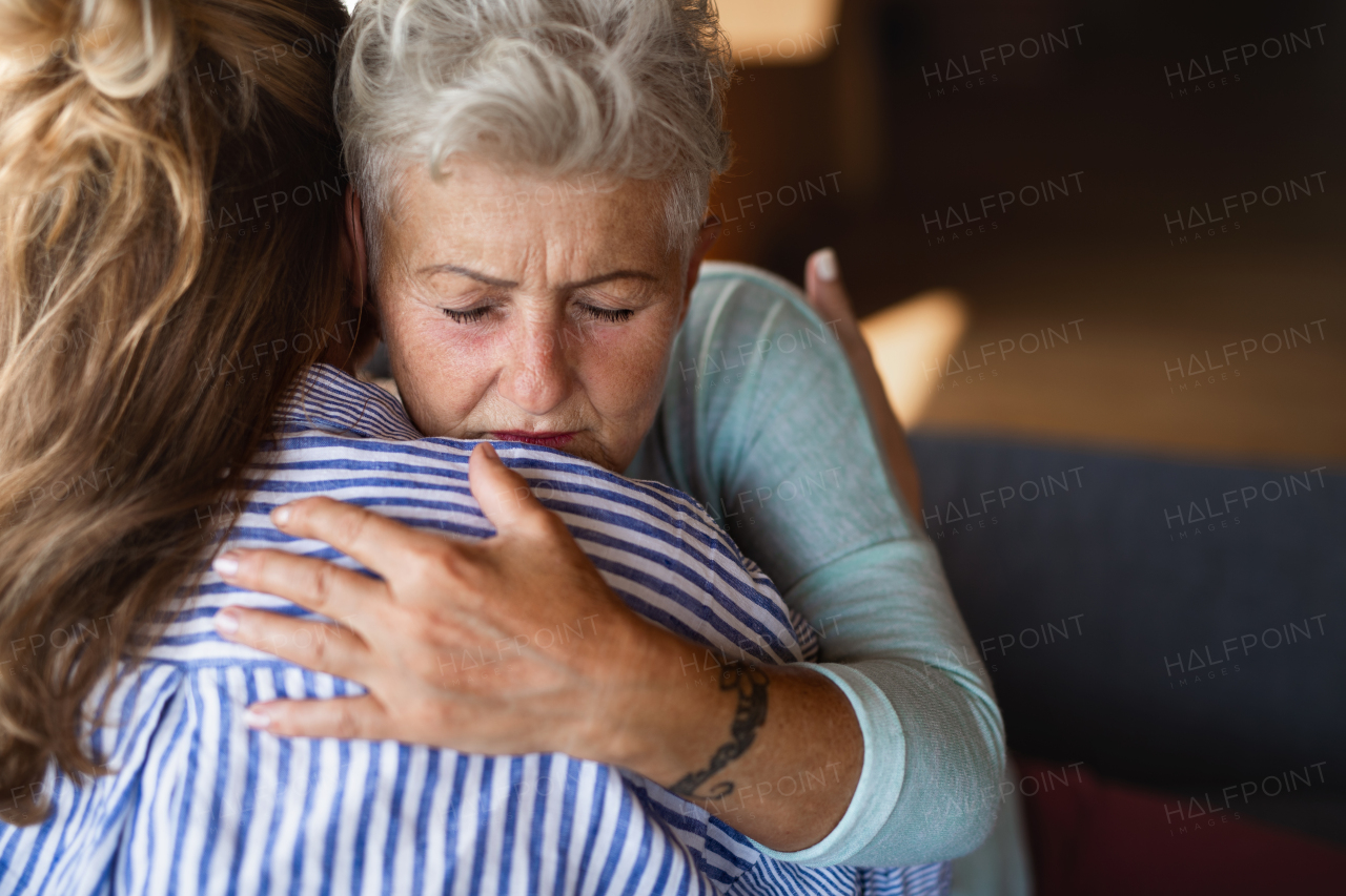 An adult daughter consoling unhappy senior mother and supporting her in struggle indoors at home.