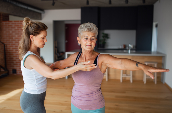 An active senior woman in sportsclothes exercising with female physioterapist indoors at home.