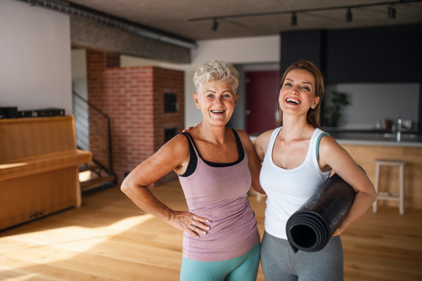 An active senior woman after workout training with adult daughter indoors at home, celebrating success.