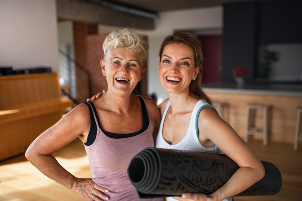 An active senior woman after workout training with adult daughter indoors at home, looking at camera.