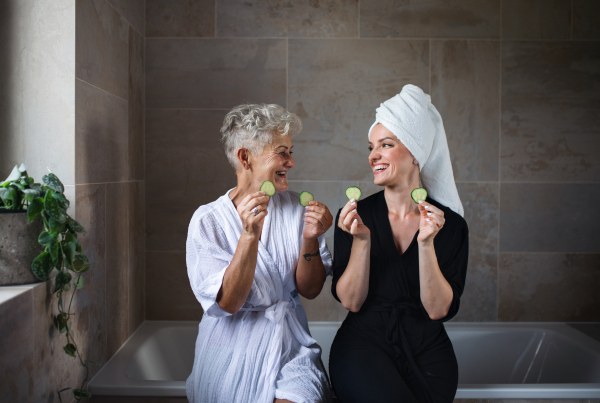 A happy senior mother in bathrobe with adult daughter indoors at home, selfcare concept.