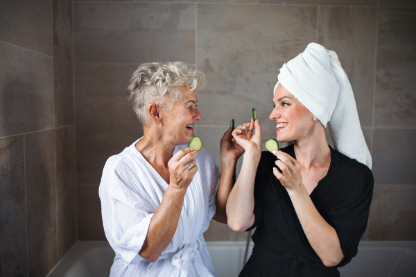 A happy senior mother in bathrobe with adult daughter indoors at home, selfcare concept.