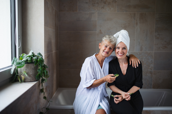 A happy senior mother in bathrobe with adult daughter indoors at home, selfcare concept.