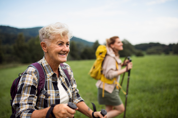 A happy mid adult woman with trekking poles hiking with active senior mother outdoors in nature.